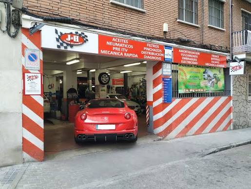 Fachada de J&H Taller Multimarca con sus características franjas diagonales rojas y blancas y un coche deportivo rojo saliendo del taller